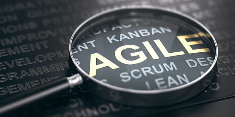 3D illustration of many words over black background and a magnifying glass with focus on the word agile.